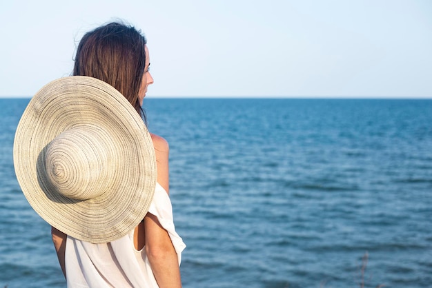 Young woman with hat standing with her back sits at the sea.