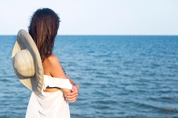 Young woman with hat standing with her back sits at the sea