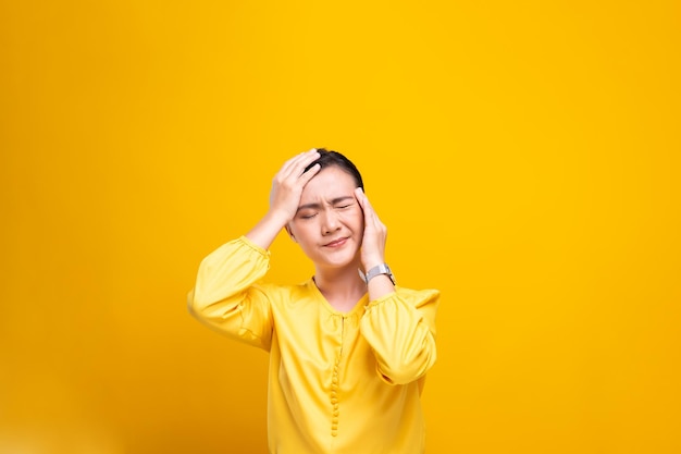 Young woman with headache against yellow background