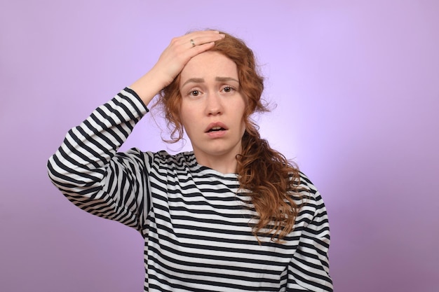 A young woman with a headache is standing on a purple background.