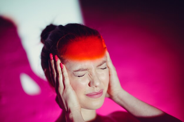 Young woman with headache and red color forehead.