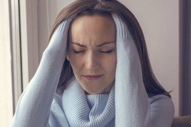 Photo young woman with a headache on the windowsill near the window at home, closeup