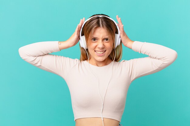 Giovane donna con le cuffie che si sente stressata, ansiosa o spaventata, con le mani sulla testa