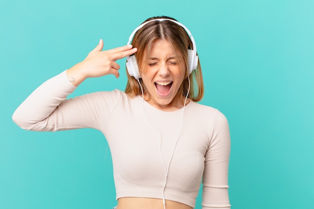 Young woman with headphones looking unhappy and stressed, suicide gesture making gun sign