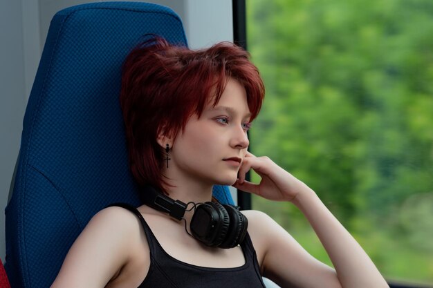 Young woman with headphones rides in a moving suburban train and looks out the window