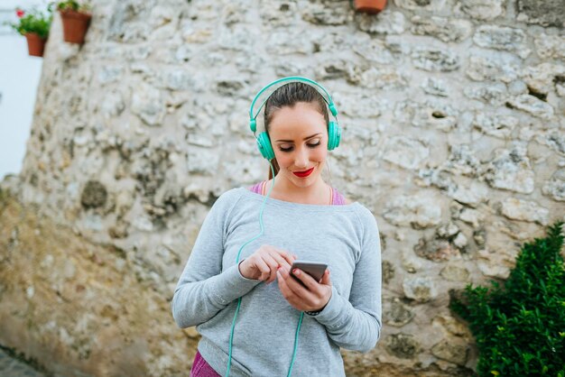 Photo young woman with headphones sending message with mobile phone