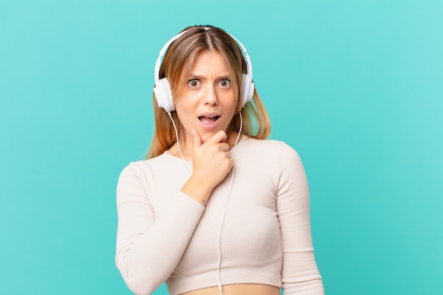 Young woman with headphones with mouth and eyes wide open and hand on chin