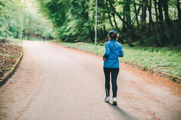 Young woman with headset running in city park copy space