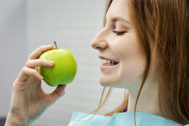 Молодая женщина со здоровым зубом кусает зеленое яблоко