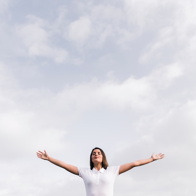 Young woman with her closed eyes outstretching her hands against blue sky