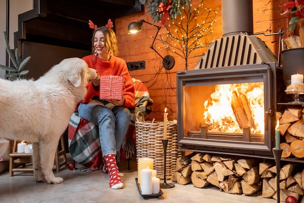 Young woman with her cute white dog during a happy New Year holidays sitting by a fireplace at home