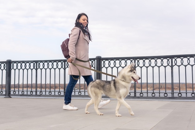 Young woman with her husky dog walking along the embankment on an autumn day