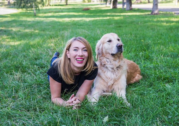 Young woman with her retriever lie on the grass in the park