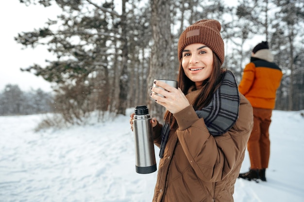 Young woman with hot drink thermos at winter forest