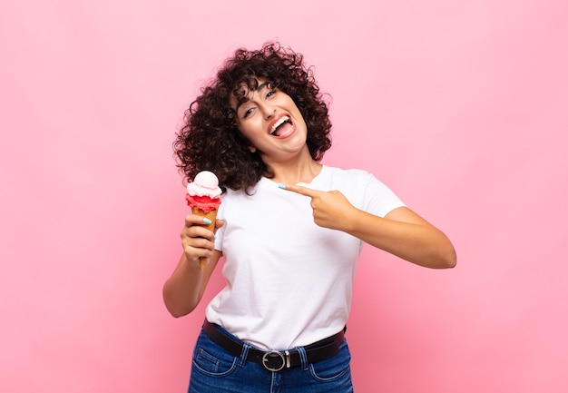 Young woman with an ice cream looking excited and surprised pointing to the side and upwards to copy space