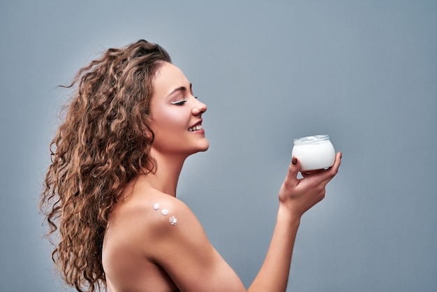 Young woman with jar of body cream on grey background Copy space