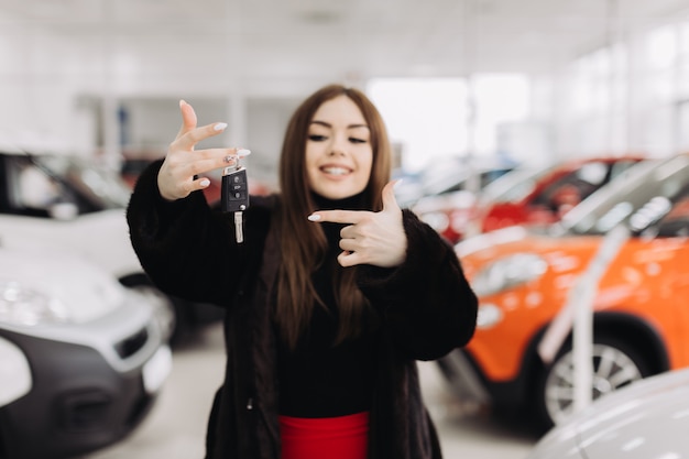 A young woman with the keys to her new car in a car store