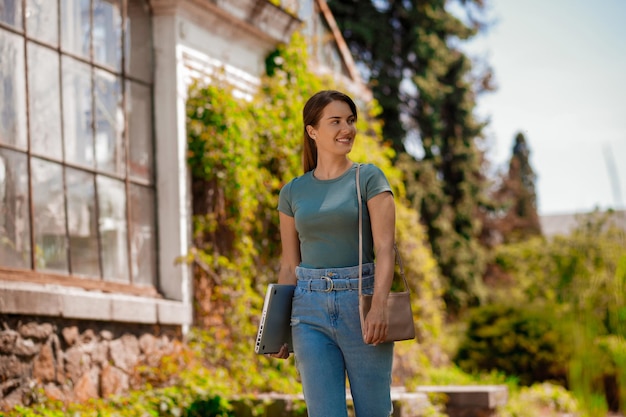 Young woman with a laptop in hands walking in the park