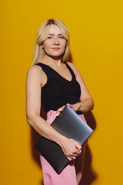 A young woman with a laptop poses on a yellow background business shooting in the studio