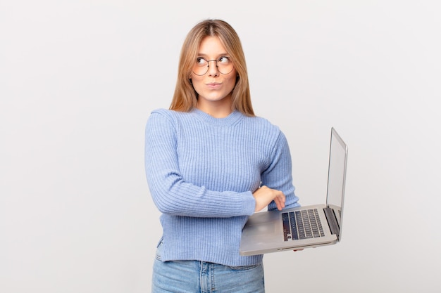 Young woman with a laptop shrugging, feeling confused and uncertain