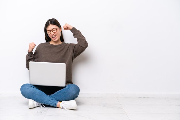 Giovane donna con un computer portatile che si siede sul pavimento per celebrare una vittoria