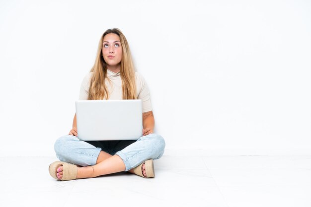 Foto giovane donna con il portatile seduto sul pavimento isolato su sfondo bianco e alzando lo sguardo