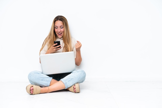 Foto giovane donna con il portatile seduto sul pavimento isolato su sfondo bianco sorpreso e l'invio di un messaggio