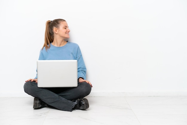 Young woman with a laptop sitting on the floor laughing in lateral position