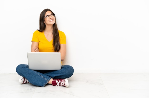 Young woman with a laptop sitting the floor looking up while smiling