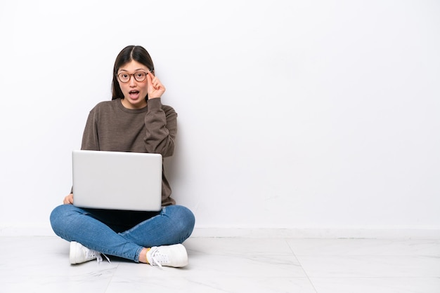 Young woman with a laptop sitting on the floor with glasses and surprised