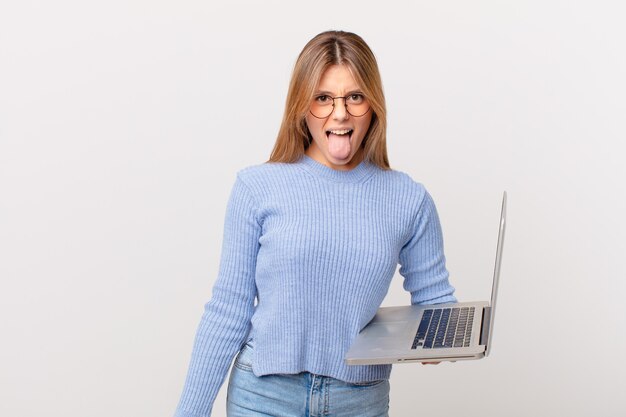 young woman with a laptop with cheerful and rebellious attitude, joking and sticking tongue out