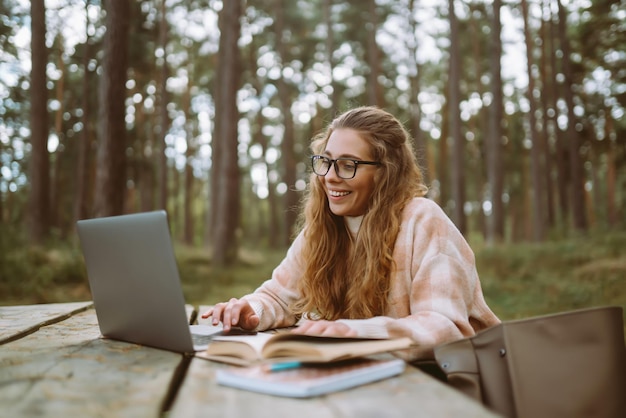 Молодая женщина с ноутбуком работает или учится в Интернете на открытом воздухе Бизнес-блогирование видеоконференция