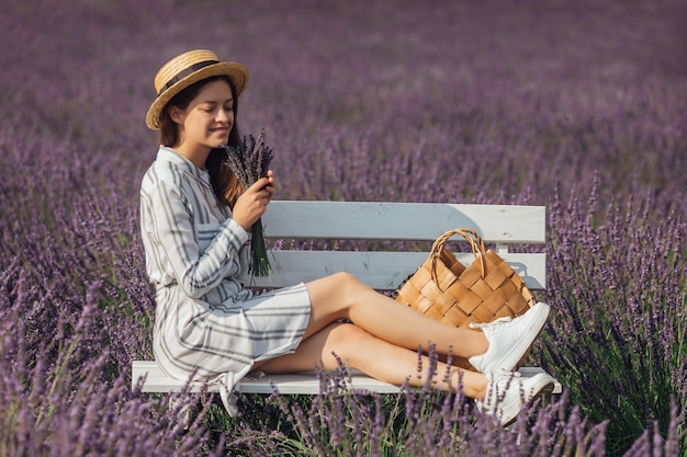 紫の花フィールドの背景にラベンダーの花束を持つ若い女性