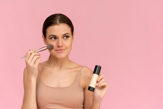 Young woman with liquid foundation Photo of woman with perfect makeup on pink background Beauty