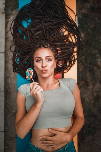 Young woman with long afro braids having fun and pouting her lips on the colorful bench in the park.