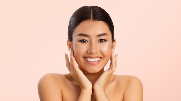 young woman with long black hair smiling touching her face