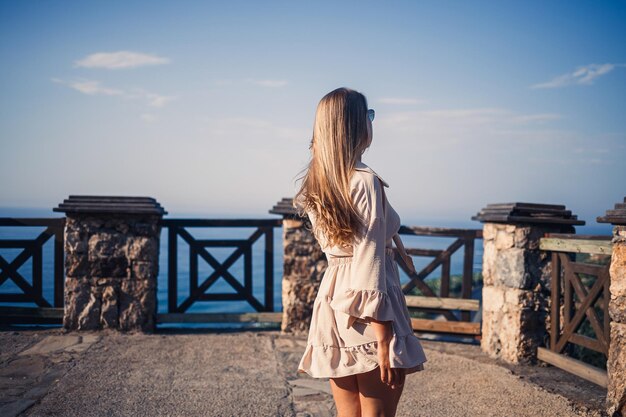 A young woman with long blond hair in a top and a skirt is walking on a summer sunny day Happy girl with a smile on her face and in sunglasses is walking on a sunny day