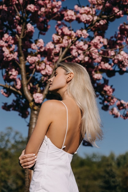 Giovane donna con lunghi capelli biondi all'aperto in un parco sul ciliegio in fiore sfondo