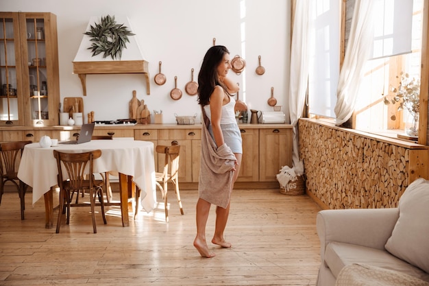 молодая женщина с длинными каштановыми волосами стоит дома на кухне в пижаме ночной рубашки