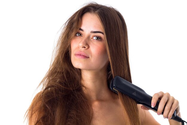 Young  woman with long brown hair using hair straightener on white background in studio