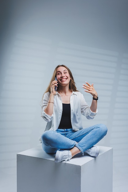 Giovane donna con lunghi capelli castani che indossa una camicia bianca e jeans che parla al telefono una donna in jeans e una semplice camicia bianca con un telefono cellulare spazio di copia su sfondo bianco