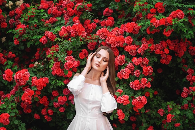 Young woman with long curly hair posing near blooming roses