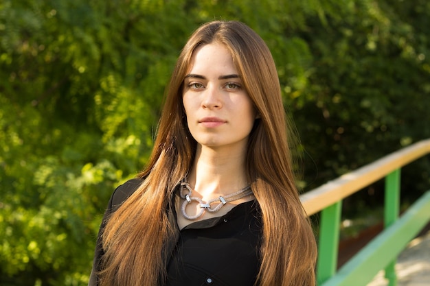 Young woman with long hair in black blouse and silver necklace on the background of green trees