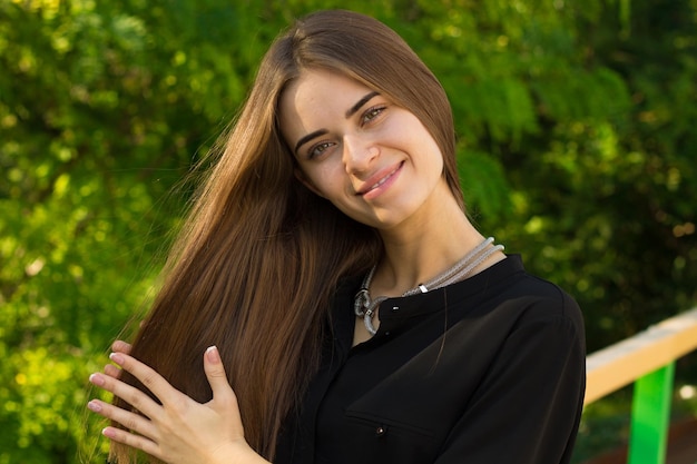 Young woman with long hair in black blouse and silver necklace on the background of green trees