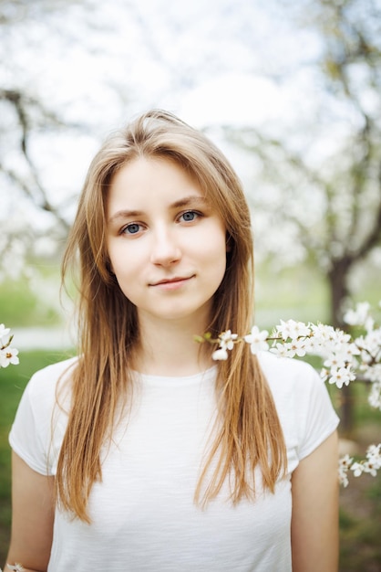 Foto giovane donna con i capelli lunghi sotto gli alberi in fiore modello di maglietta bianca della stagione primaverile