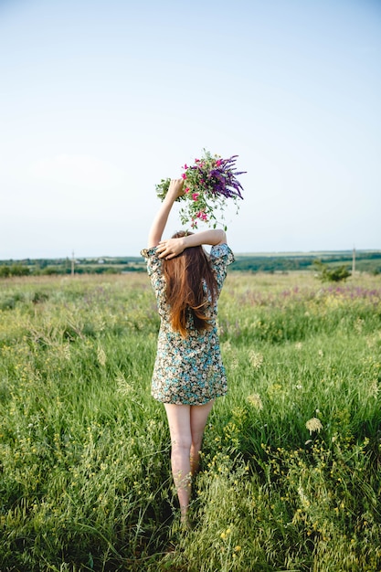 カラフルなショートドレスを着た長い髪の若い女性は、立っている挙手で花束を持っています...