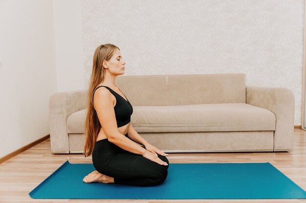 Young woman with long hair fitness instructor in black sportswear doing stretching and pilates on