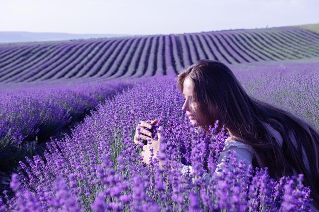 Young woman with long hair gently caress lavender bushes with hand Blooming lavender scented fields background with beautiful purple colors and bokeh lights Close up Selective focus Slow motion