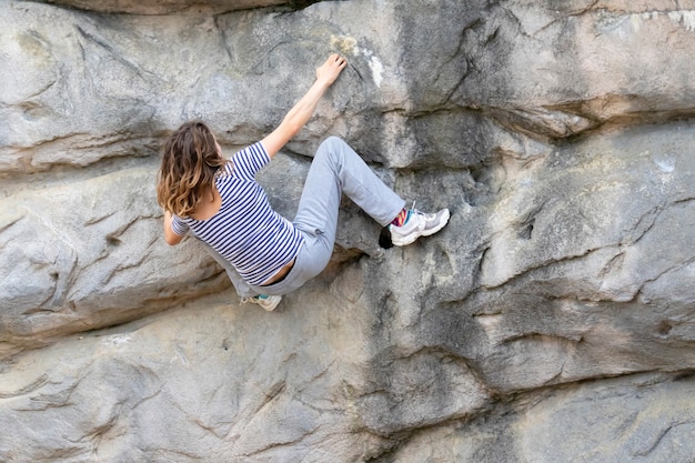 Young woman with long hair hanging on a rocky face of a\
mountain while climbing up without a rope support