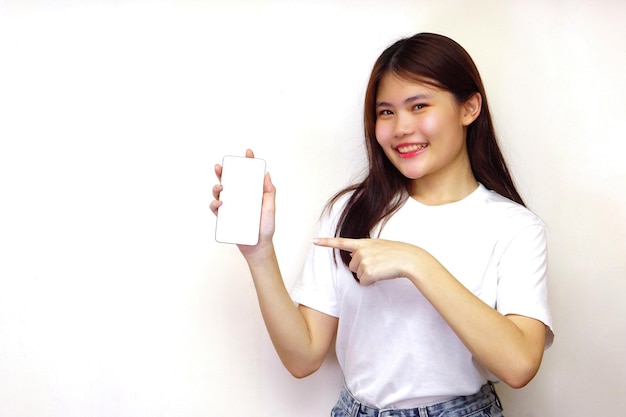 Giovane donna con i capelli lunghi che tiene lo smartphone con schermo vuoto e punta il dito verso lo smartphone